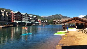 A waterfront hotel with multiple buildings, paddle boarding activities, and a sandy beach area. - Luxury 3 Bedroom Townhouse next to Keystone Lake, Free Shuttle, Hot Tub and Sauna (Keystone)