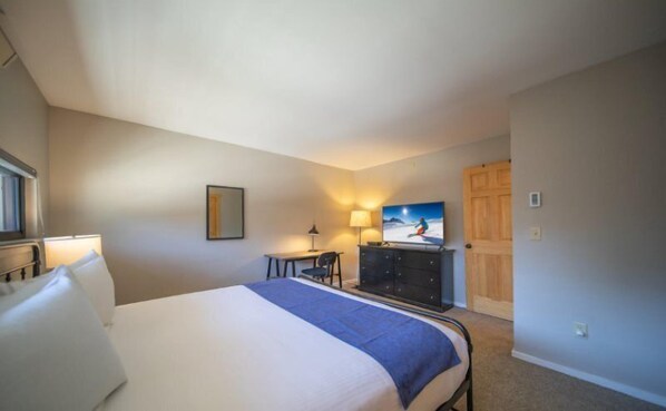 A hotel room with a bed, a desk, a chair, a dresser, and a painting on the wall.