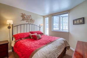 A bedroom with a large bed, two bedside lamps, a window, and a wall-mounted artwork.