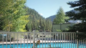 Une piscine entourée d’une clôture blanche, bordée d’arbres et avec une montagne en toile de fond.