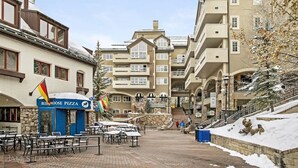 Un espacio exterior cubierto de nieve con mesas y sillas, un restaurante Blue Moose Pizza y un edificio con varios balcones.