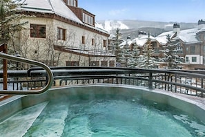 Un jacuzzi con vistas a edificios y árboles cubiertos de nieve.