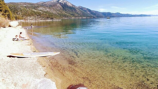 Une plage à l’eau cristalline, une planche de surf et des montagnes en arrière-plan.