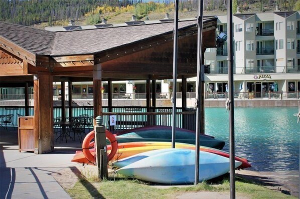 A covered outdoor seating area with a poolside view, a pizza restaurant, and colorful kayaks by the water.