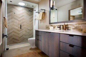 Un baño moderno con ducha de patrón geométrico de espiga, inodoro, tocador con espejo y toallero.