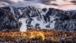 Un pueblo en la montaña, con picos nevados y un pueblo iluminado abajo.