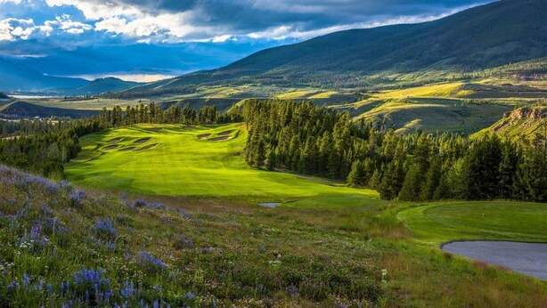 Un parcours de golf caractérisé par des collines douces, des forêts denses et un paysage montagneux en arrière-plan.