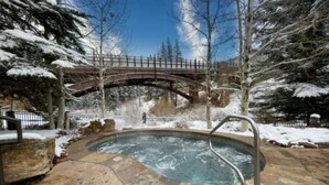 A hot tub surrounded by snow-covered trees and a stone patio. - Ski in, Ski out 2 Bedroom Vacation Rental in the Heart of Lionshead Village (Vail)
