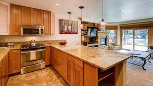 A modern kitchen with wooden cabinets, stainless steel appliances, and a granite countertop. - Ski in, Ski out 2 Bedroom Vacation Rental in the Heart of Lionshead Village (Vail)