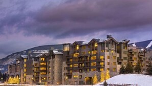 A multi-story hotel with a stone facade, multiple balconies, and a mountainous backdrop. - Vail Lion Studio Mountain Vacation Rental Just Steps From the Eagle Bahn Gondola (Vail)