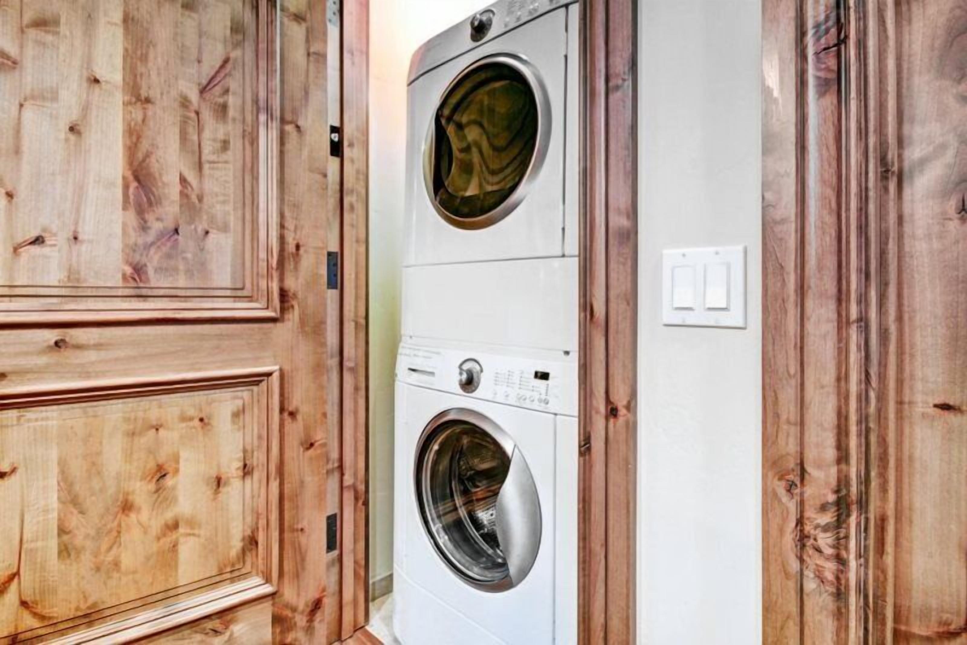 A laundry room with two stacked washing machines, wooden walls, and a white door.