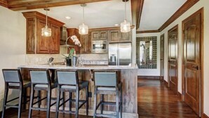 A kitchen with wooden cabinets, a central island with bar stools, pendant lighting, and stainless steel appliances. - Platinum Vail Ritz-carlton 3 Bedroom Mountain Residence Just One Block From the Eagle Bahn Gondola (Vail)