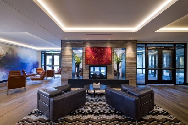 A modern lobby with leather sofas, a central fireplace, and large windows. - Vail Lion 2 Bedroom Mountain Vacation Rental Just Steps From the Eagle Bahn Gondola (Vail)