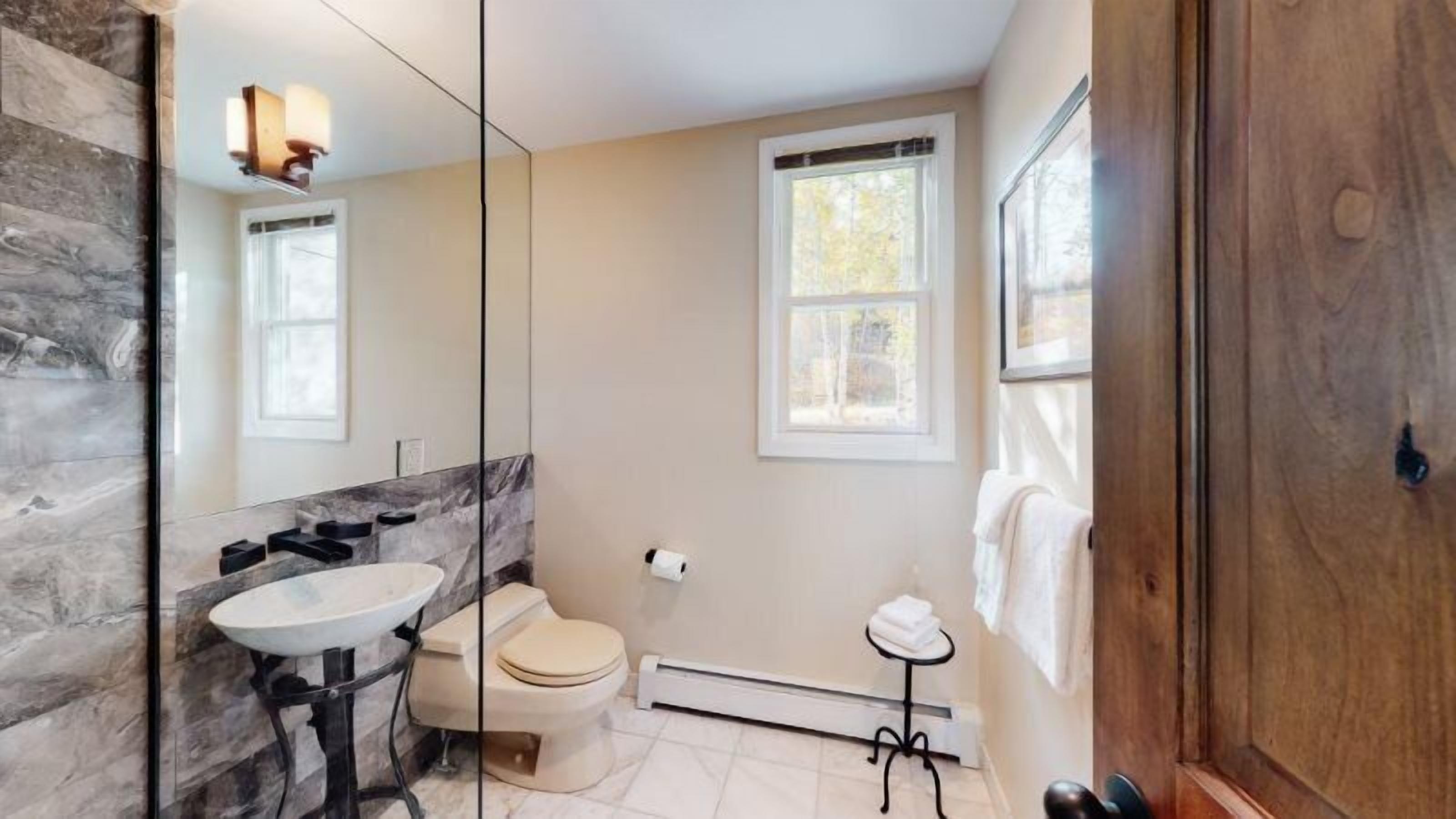 A bathroom with a marble wall, a sink, a toilet, a heater, and a window.
