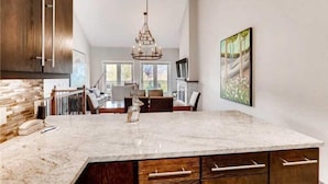 A modern kitchen with a large marble island, wooden cabinets, and a chandelier. - 2 Bedroom Ski-in Ski-out Condo in Snowmass Village (Snowmass Village)
