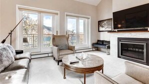 A living room with a fireplace, a sofa, a chair, a coffee table, and a TV mounted on the wall. - 2 Bedroom Ski-in Ski-out Condo in Snowmass Village (Snowmass Village)