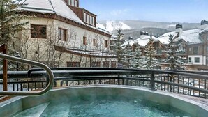 A hot tub with a view of snow-covered buildings and trees.