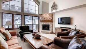A spacious living room with a fireplace, large windows, and a flat-screen TV.