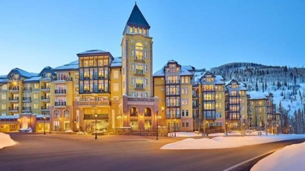 Un hôtel à plusieurs étages, doté d’une tour imposante, entouré d’un paysage enneigé et dont la façade est bien éclairée.