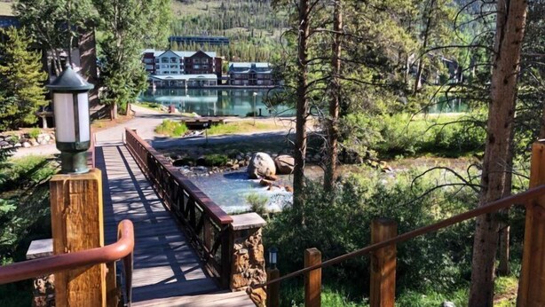 Un puente de madera que lleva a una cabaña con vista a un lago y un bosque.