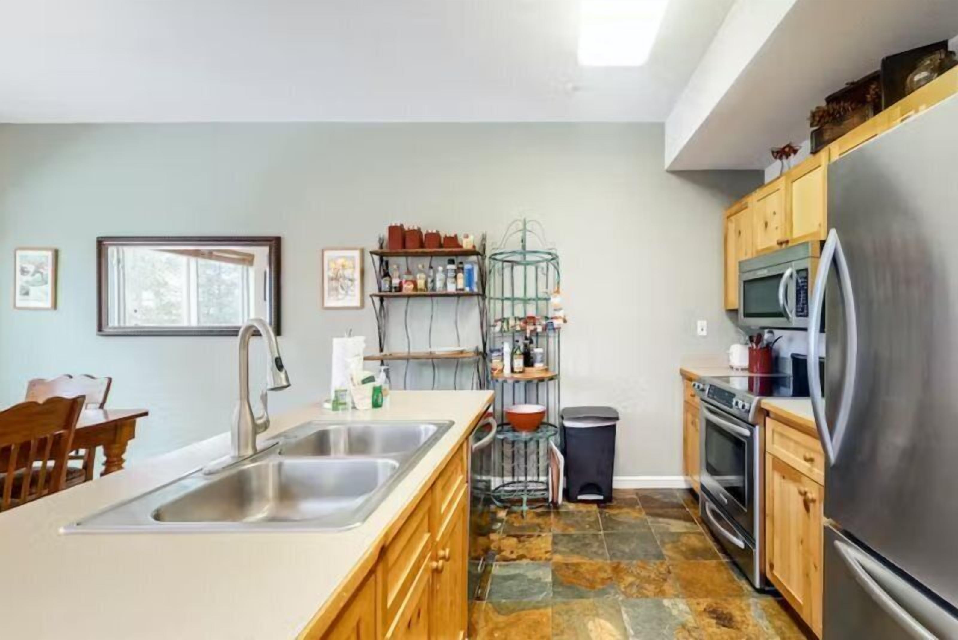A kitchen with a large island, stainless steel appliances, wooden cabinets, and a tiled floor.