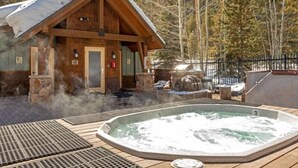 Una cabaña de madera con jacuzzi y zona de estar al aire libre rodeada de árboles.
