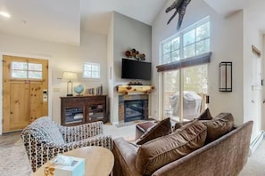 A spacious living room with a fireplace, a large window, and a television mounted on the wall. - Seasons 3 Bedroom Townhome in Lakeside Village (Keystone)