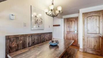 A wooden bench with a bowl, a chandelier, and a door in a room with white walls and a wooden floor.
