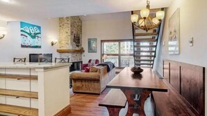 A spacious living area with a wooden dining table, a sofa, and a kitchen area with a stone wall. - Luxury Ski In, Ski Out 1 Bedroom Condo in Lionshead Village (Vail)