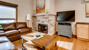 A living room with a stone fireplace, leather sofa, wooden coffee table, and a television. - Luxury Ski In, Ski Out 1 Bedroom Condo in Lionshead Village (Vail)