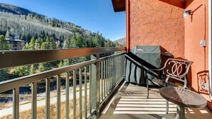 A balcony with a view of a forested mountain, a grill, and outdoor furniture. - Luxury Ski In, Ski Out 1 Bedroom Condo in Lionshead Village (Vail)