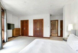 A spacious hotel room with a large bed, wooden wardrobe, a flat-screen TV, and a door leading to another room. - Platinum Vail Solaris 3 Bedroom With Den Vacation Rental Set at the Base of the Mountain Just Steps From the Gondola (Vail)