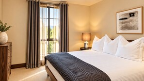 A hotel room with a large bed, a nightstand with a lamp, a window with curtains, and a framed picture on the wall. - Platinum Vail Solaris 4 Bedroom Vacation Rental Set at the Base of the Mountain Just Steps From the Gondola (Vail)
