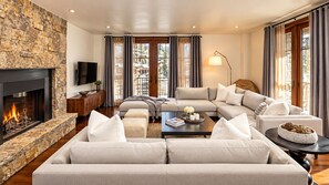 A modern living room with a stone fireplace, a sectional sofa, a coffee table, and a television. - Platinum Vail Solaris 4 Bedroom Vacation Rental Set at the Base of the Mountain Just Steps From the Gondola (Vail)