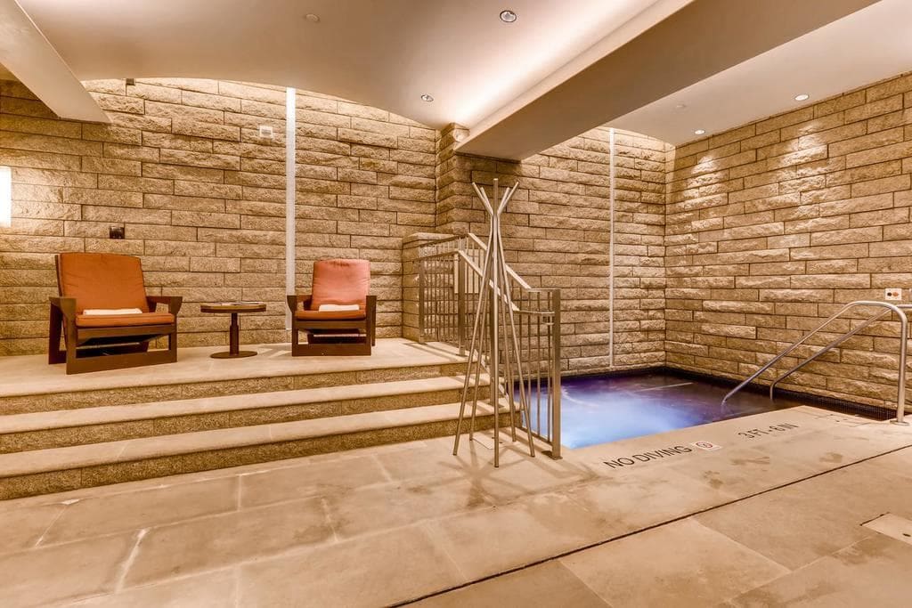 Un'area benessere con parete in pietra, vasca idromassaggio e sedute.
