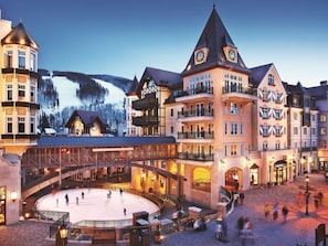 A hotel with a central ice rink, multiple floors, and a mountainous backdrop. - Platinum 3 Bedroom Vacation Rental in the Heart of Vail (Vail)