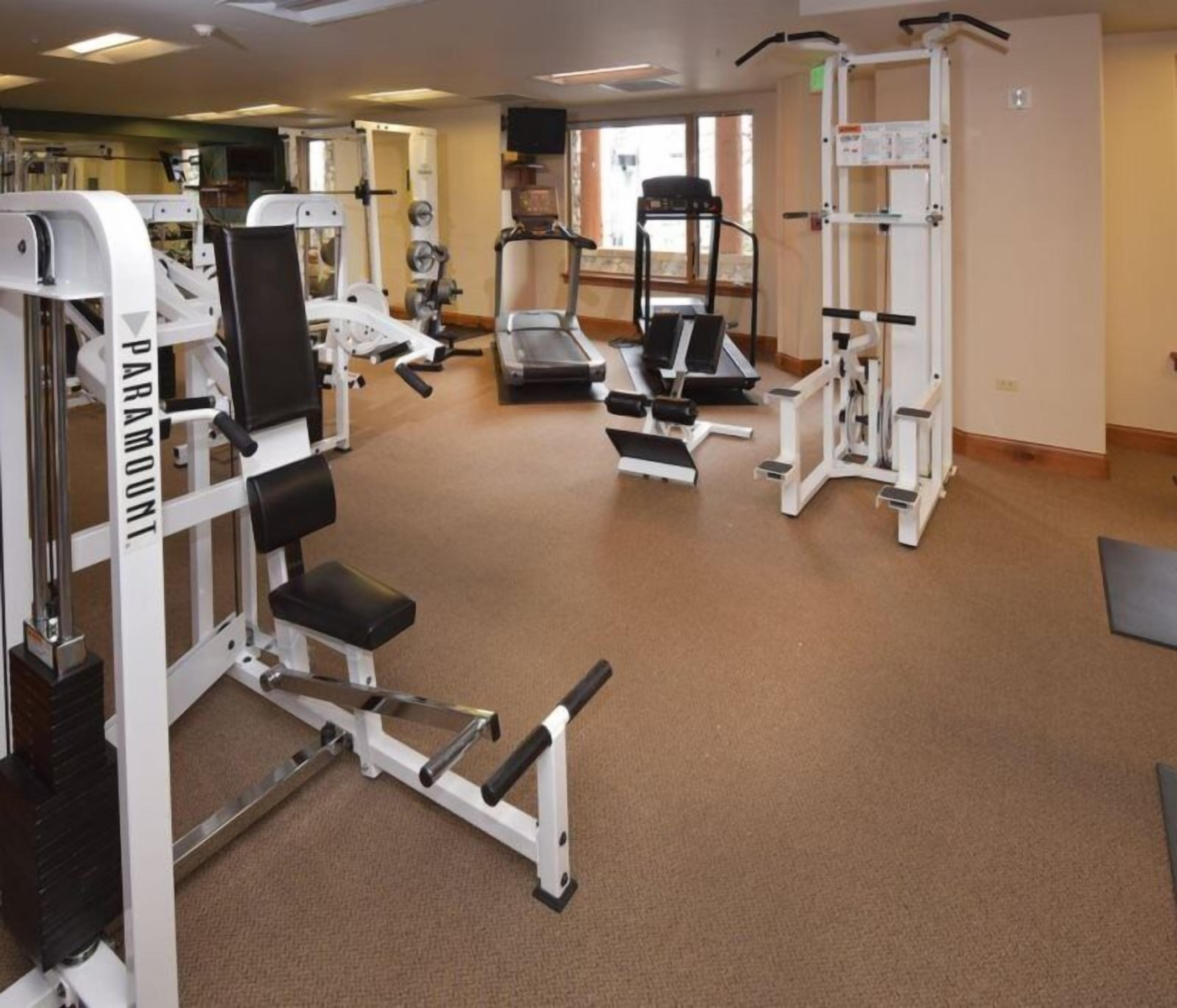 A gym with various exercise equipment including weight machines, treadmills, and a stair climber.