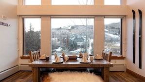Ein Essbereich mit Holztisch, gedeckt für vier Personen, großen Fenstern mit Blick auf eine verschneite Landschaft und an der Wand befestigten Skiern.