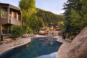 A pool area with lounge chairs and umbrellas, surrounded by trees and a mountain backdrop.