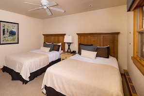 A hotel room with two beds, a ceiling fan, a nightstand, a lamp, and a framed picture on the wall.