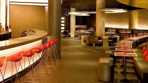 Un restaurante moderno con una barra curva, sillas rojas y una variedad de arreglos de asientos, incluyendo mesas y cabinas.
