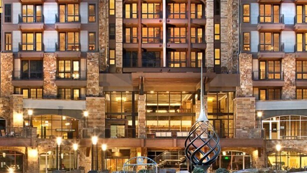 Un hotel de varios pisos con fachada de piedra, amplias ventanas y una entrada central con una escultura singular.