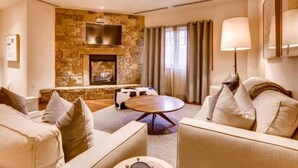Una sala de estar moderna con una pared de piedra, una chimenea, un televisor de pantalla plana y una mesa de centro redonda.