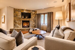 A living room with a stone fireplace, a flat-screen TV, and a round coffee table.