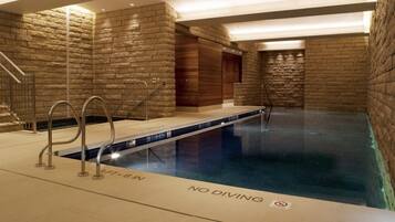 Una piscina interior con un cartel de prohibición de saltos, paredes de piedra y una puerta de madera.