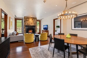 A modern living room with a fireplace, a dining area, and a large window overlooking greenery.