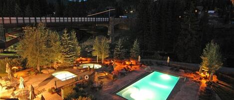 A pool area with a hot tub, lounge chairs, and a bridge in the background.