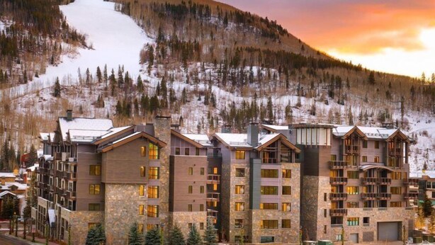 A multi-story hotel with a stone facade, balconies, and a view of a snowy mountain slope. - Vail Lion 1 Bedroom Mountain Vacation Rental Just Steps From the Eagle Bahn Gondola (Vail)