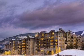 A multi-story hotel with a stone facade, multiple balconies, and a mountainous backdrop.