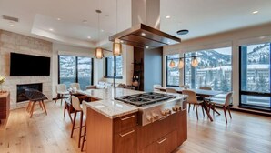 A modern kitchen with a central island, large windows offering mountain views, and a fireplace. - Vail Lion 1 Bedroom Mountain Vacation Rental Just Steps From the Eagle Bahn Gondola (Vail)